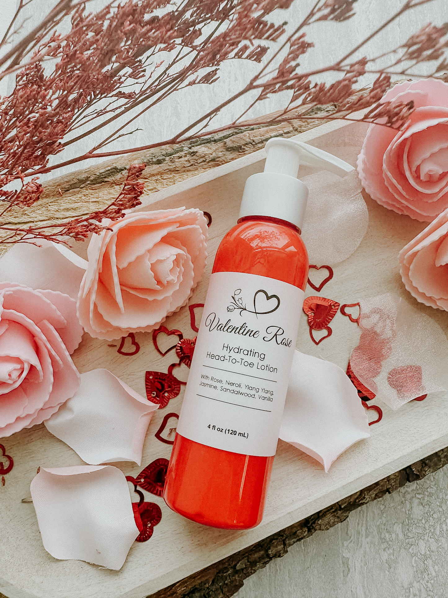 Valentine Rose hydrating hand and toe lotion bottle with pink roses and dried flowers on a wooden surface.