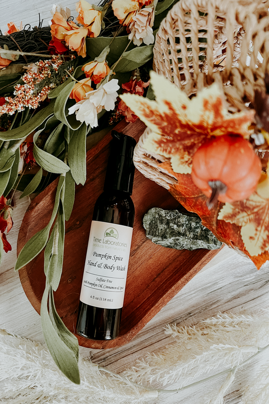 Bottle of pumpkin spice hand and body wash on a wooden tray with decorative flowers and leaves.